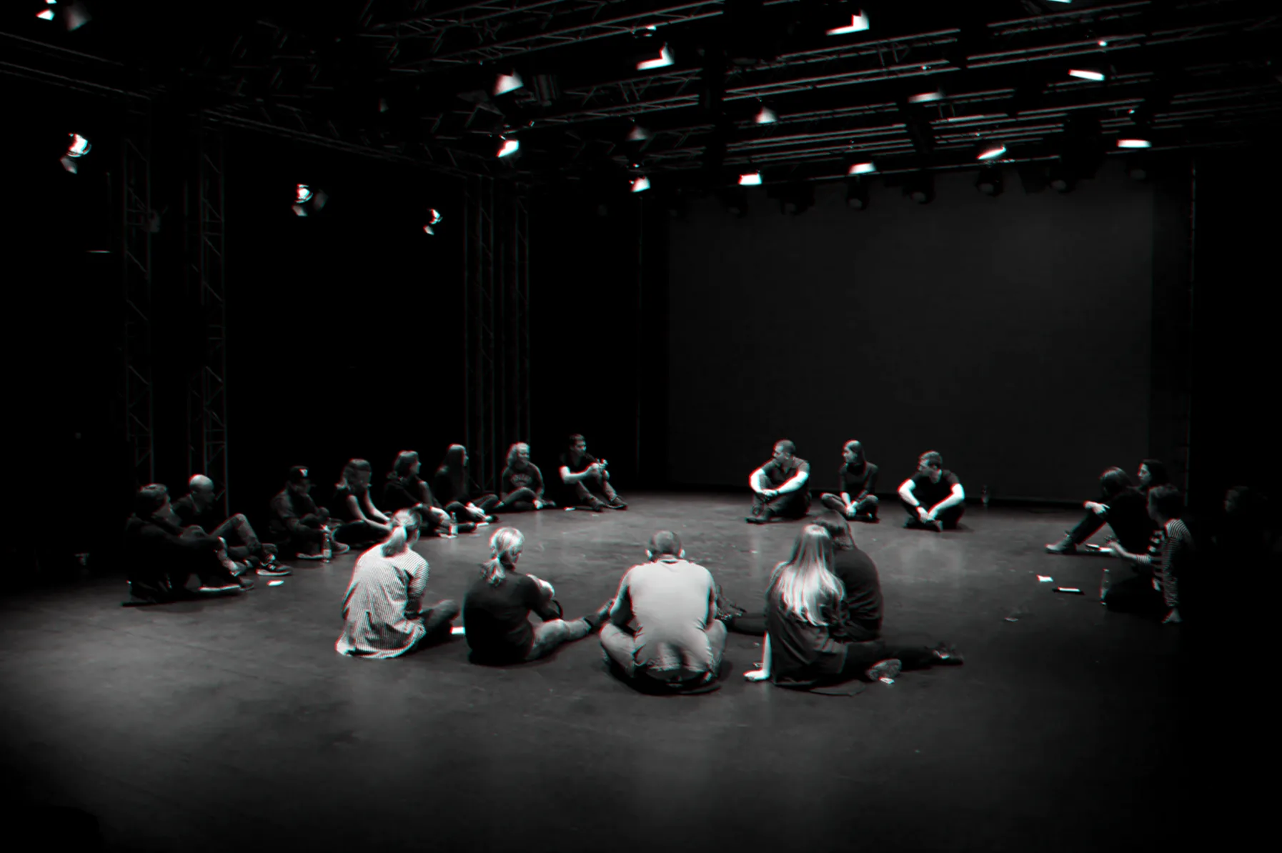 Participants sitting in a circle on a dark stage under a single light